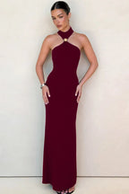 Woman in a burgundy halter neck maxi dress with a gold ring detail at the neckline.