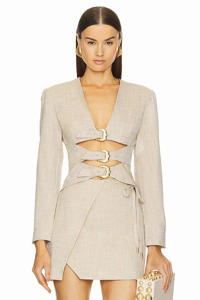 Woman wearing a beige linen blend blazer with cut-out detailing and gold buckle closures, paired with a matching wrap skirt.