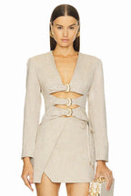 Woman wearing a beige linen blend blazer with cut-out detailing and gold buckle closures, paired with a matching wrap skirt.