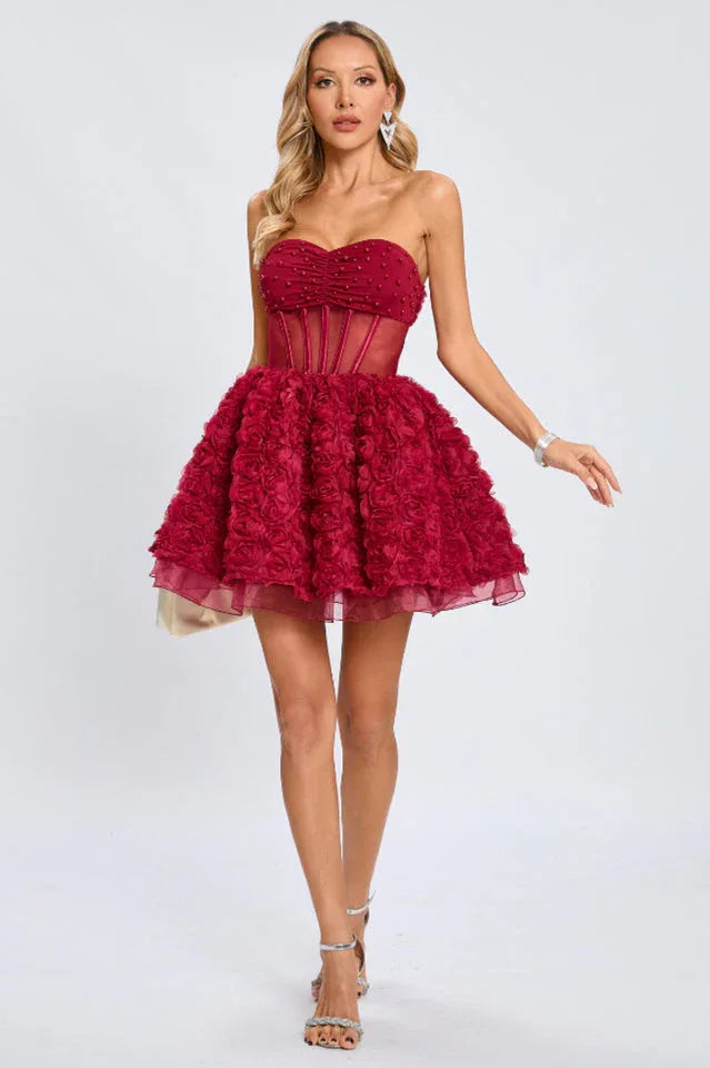 Woman standing in a strapless red cocktail dress with a corset waist and a textured rose skirt, showcasing the full silhouette.