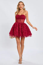 Woman standing in a strapless red cocktail dress with a corset waist and a textured rose skirt, showcasing the full silhouette.