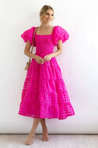 Full-length view of a woman in a vibrant pink smocked midi dress with a square neckline.