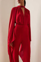 Close-up of the red crepe wide leg jumpsuit, highlighting the draped cape sleeves and keyhole neckline.