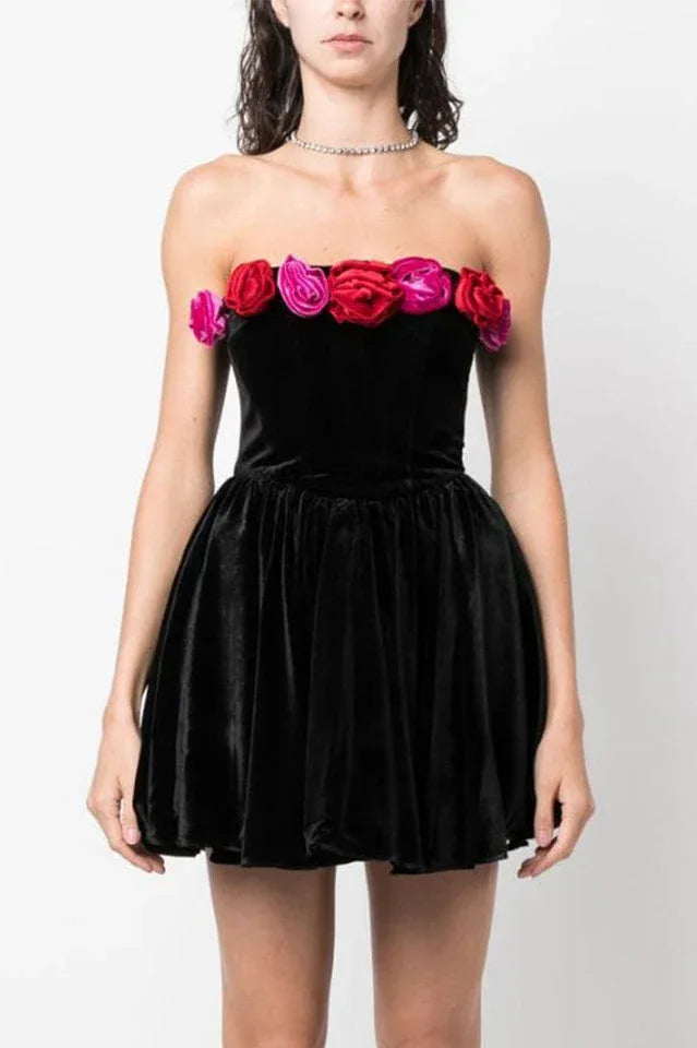 Front view of a woman in a black strapless velvet dress with a floral trim and a full skirt.