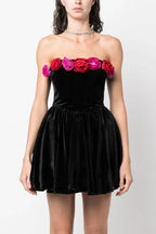 Front view of a woman in a black strapless velvet dress with a floral trim and a full skirt.