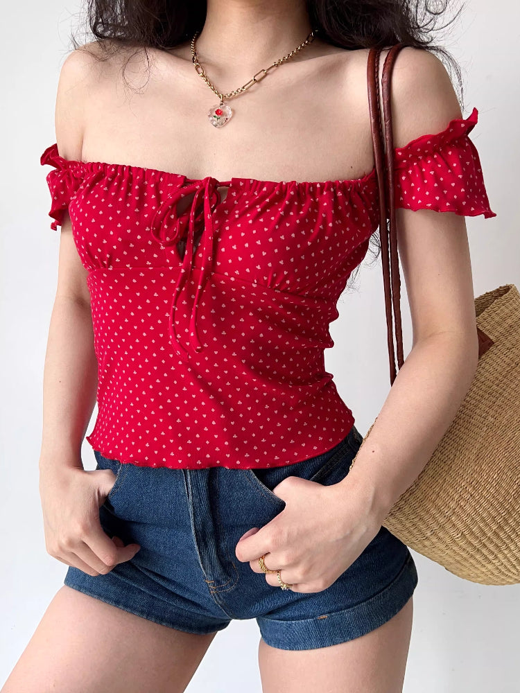 Woman in a red off-the-shoulder top with heart print and denim shorts.