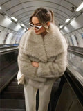 woman on an escalator wearing a light grey faux fur jacket and white sunglasses