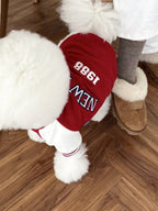 Close-up of the back of a white Bichon Frise dog wearing a red "New York 1988" jacket.