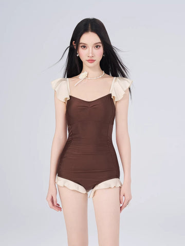 Woman wearing a brown and cream one-piece swimsuit with flutter sleeves and a skirted bottom.