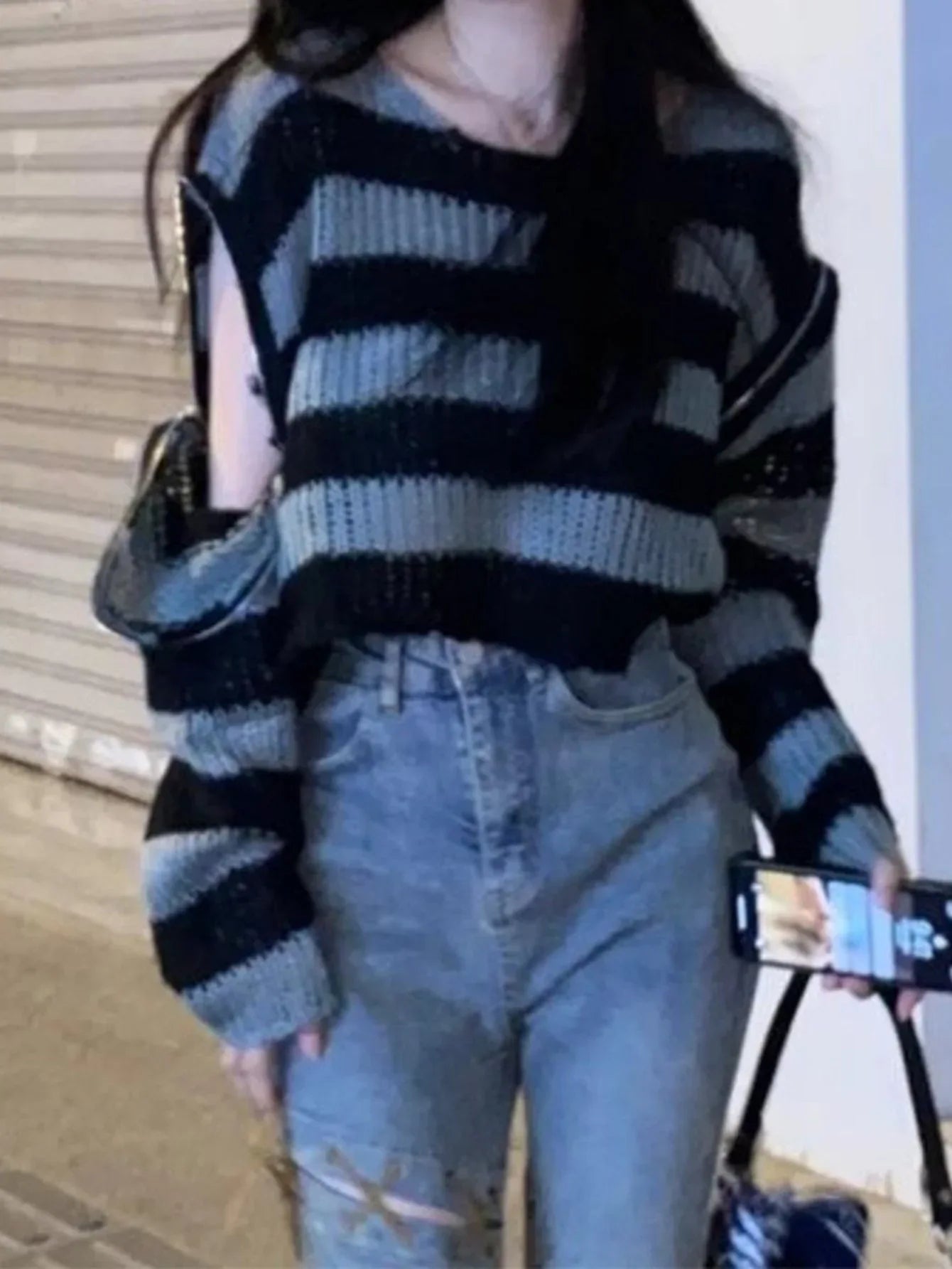 Woman in a grey and black striped cropped knit sweater with zippered sleeves, styled with light wash jeans.