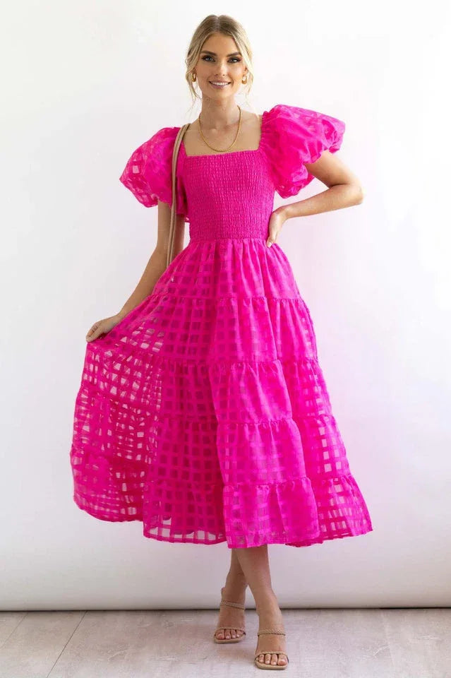 Woman wearing a bright pink midi dress with puff sleeves and a tiered skirt. Main image