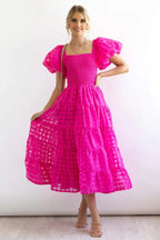 Woman wearing a bright pink midi dress with puff sleeves and a tiered skirt.