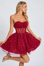 Full-body view of a woman modeling a short, strapless red formal dress with a fitted bodice and a voluminous rose-appliqued skirt.