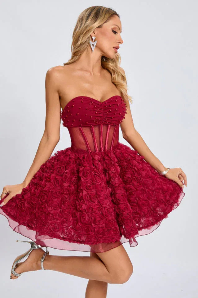 Full-body view of a woman modeling a short, strapless red formal dress with a fitted bodice and a voluminous rose-appliqued skirt.