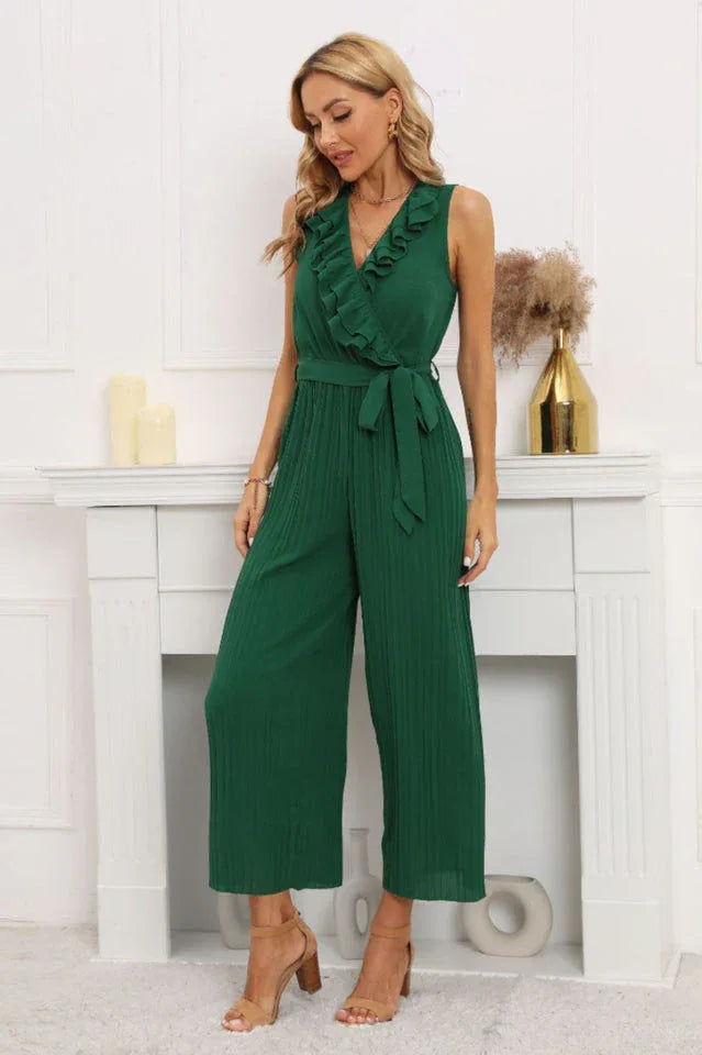 Full body shot of a woman in a green sleeveless pleated jumpsuit with a ruffled V-neck.