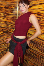Back view of a woman wearing a burgundy one-shoulder draped top with light blue textured shorts.