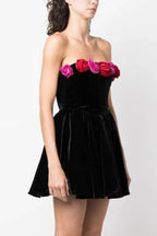 Side view of a woman wearing a black strapless velvet dress with a floral trim and a full skirt.
