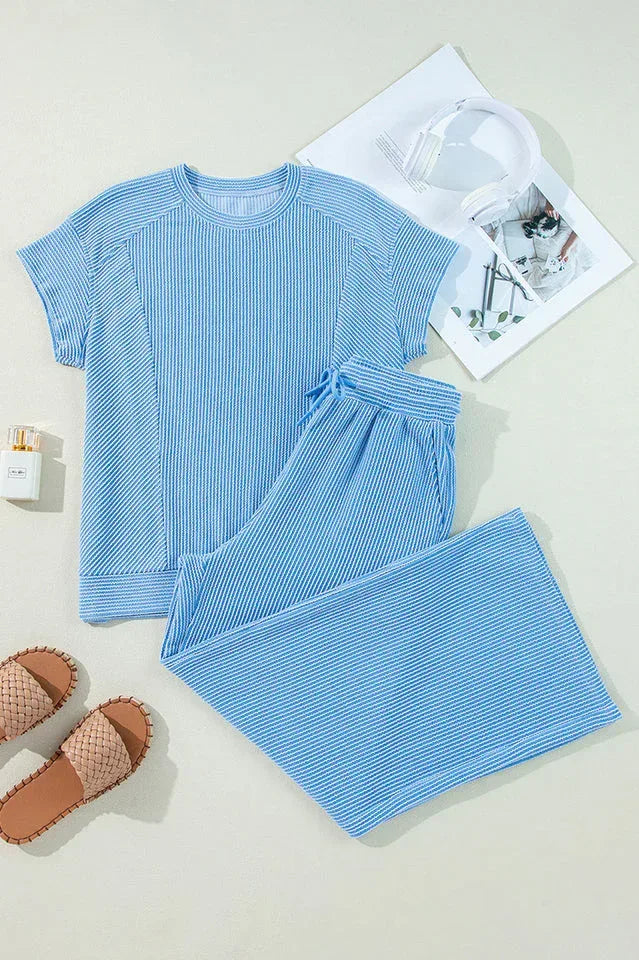 Flat lay of a blue ribbed knit short sleeve top and wide leg pants with accessories