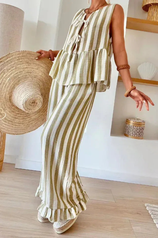 Woman holding a straw hat while wearing a striped peplum top and pants