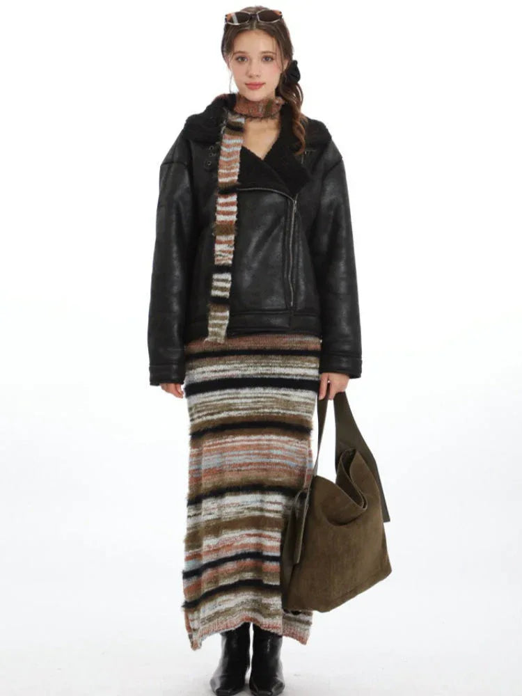 Woman wearing a black faux leather aviator jacket with a shearling collar, striped maxi skirt, and olive green shoulder bag.