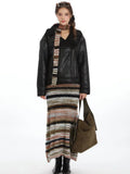 Woman wearing a black faux leather aviator jacket with a shearling collar, striped maxi skirt, and olive green shoulder bag.