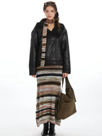 Woman wearing a black faux leather aviator jacket with a shearling collar, striped maxi skirt, and olive green shoulder bag.