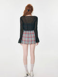 Back view of a woman wearing a black sheer bell sleeve cardigan and a red and blue plaid spaghetti strap mini dress.