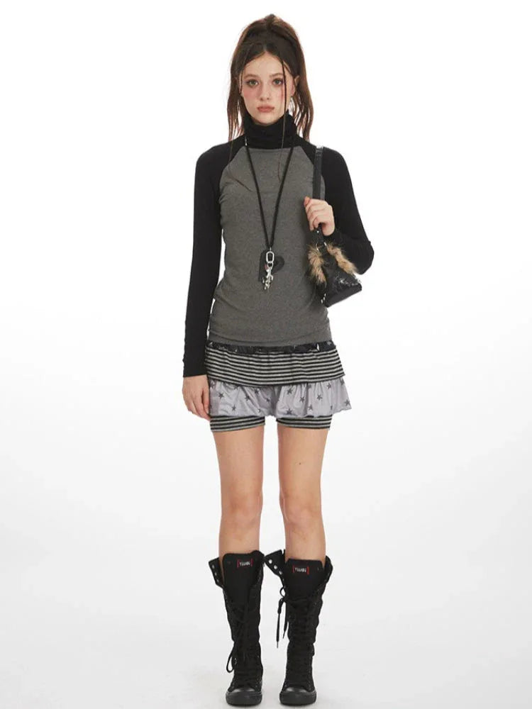 Woman wearing a grey long-sleeved turtleneck top with black raglan sleeves, layered grey and black striped shorts with a subtle star print, and black lace-up boots.