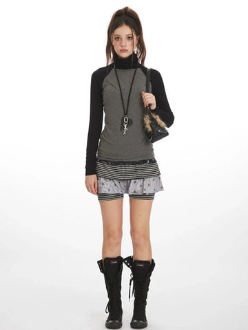 Woman wearing a grey long-sleeved turtleneck top with black raglan sleeves, layered grey and black striped shorts with a subtle star print, and black lace-up boots.