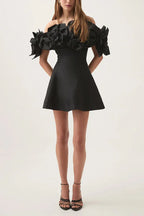 Woman in a black off-the-shoulder dress with dramatic floral sleeves and a flared skirt, paired with black heels.