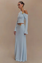 Woman wearing a light blue long-sleeved cropped top and a floor-length light blue skirt with a floral embellishment on the shoulder and hip.