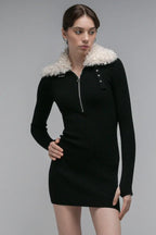 Model wearing a black long sleeve ribbed knit mini dress with a white faux fur collar and a silver zipper front.