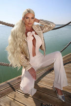 Woman in a light pink ruched jumpsuit with a plunging neckline and floral details, kneeling on a wooden deck.