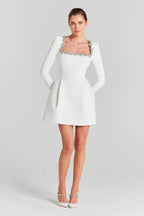 Full-body view of a woman in a white A-line dress with long sleeves and crystal embellishments