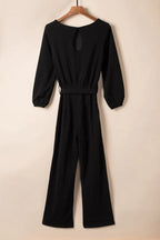 Back view of a black long sleeve wide leg jumpsuit with a tie waist and keyhole detail, displayed flat.