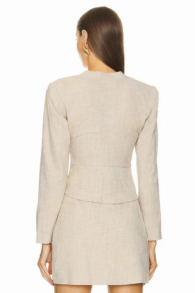 Back view of a woman wearing a beige linen blend blazer with a fitted silhouette and a wrap skirt.