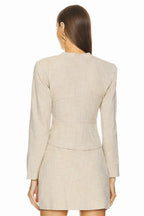 Back view of a woman wearing a beige linen blend blazer with a fitted silhouette and a wrap skirt.