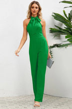 Woman wearing a green wide leg halter neck jumpsuit with a bow detail