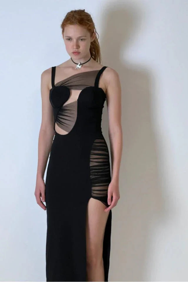 Woman in a black asymmetrical maxi dress with a high slit and cut-outs.