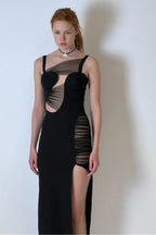 Woman in a black asymmetrical maxi dress with a high slit and cut-outs.