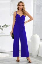 Woman in a royal blue wide leg jumpsuit with spaghetti straps and a cowl neckline.