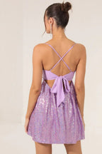 Woman from behind wearing a lavender sequined fit and flare party dress with spaghetti straps and a tie-back detail.