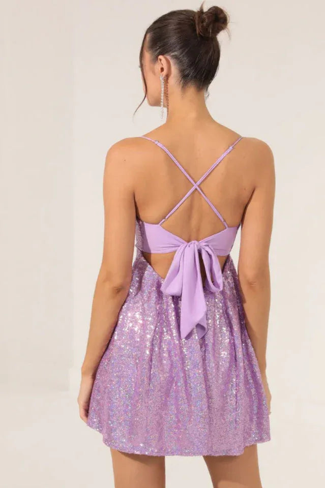 Woman from behind wearing a lavender sequined fit and flare party dress with spaghetti straps and a tie-back detail.