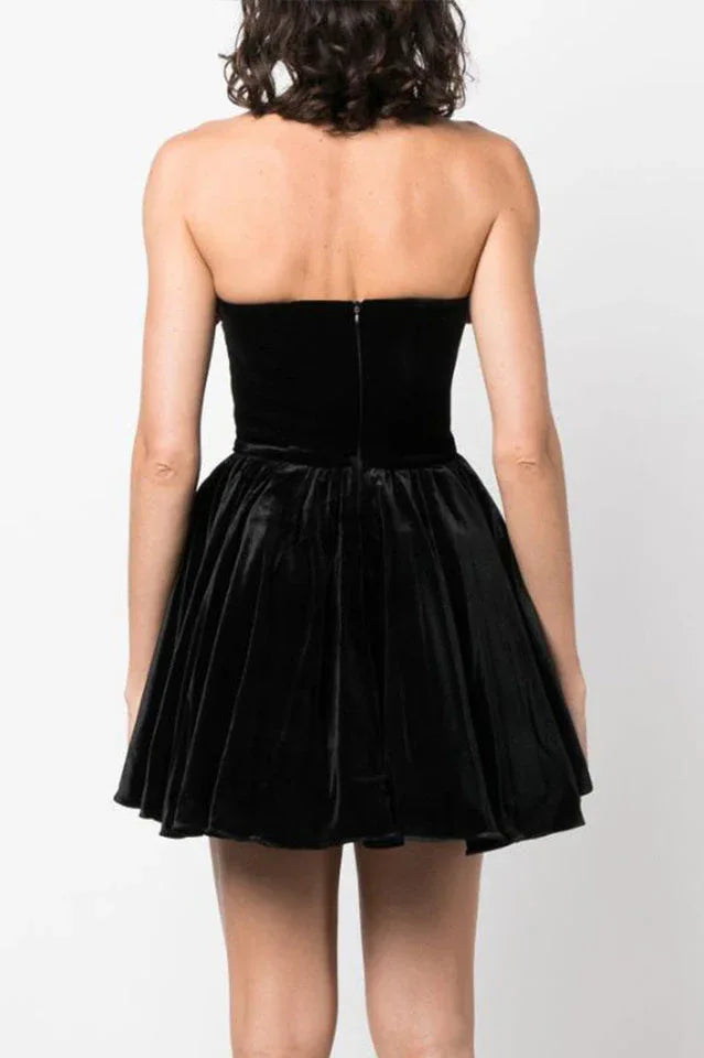 Back view of a woman in a black strapless velvet dress with a floral trim and a full skirt, showing the zipper closure.