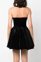 Back view of a woman in a black strapless velvet dress with a floral trim and a full skirt, showing the zipper closure.