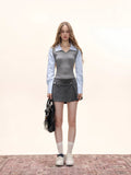 Full-body view of a model in a grey vest and striped shirt ensemble with a pleated skirt, holding a black handbag.