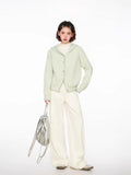Full body view of a woman in a light green hooded cardigan, white top, and cream wide-leg pants.