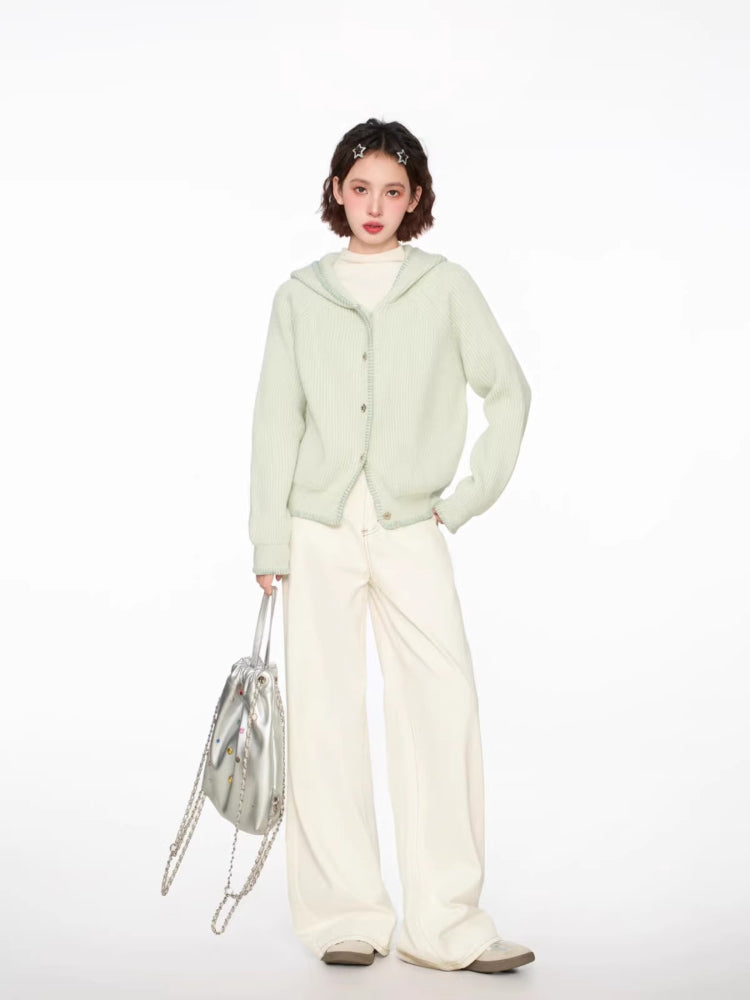 Full body view of a woman in a light green hooded cardigan, white top, and cream wide-leg pants.