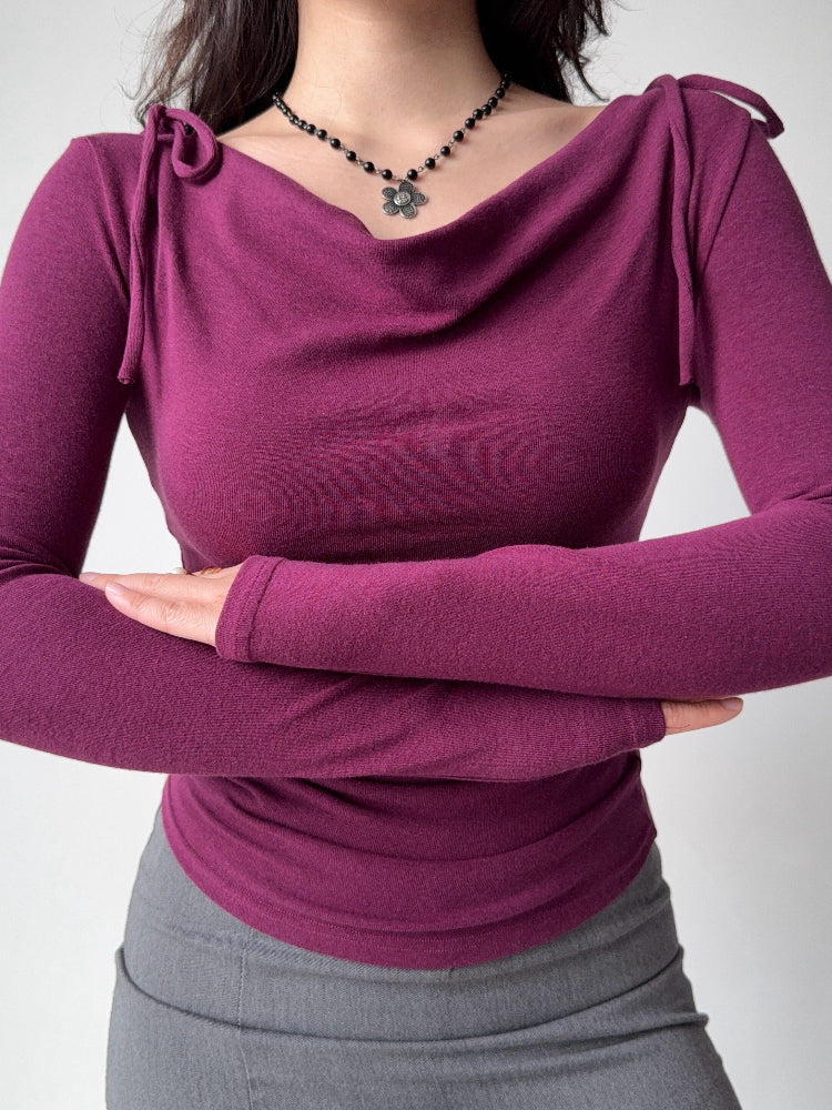 Woman wearing a plum long-sleeve top with a draped neckline and tie shoulder details.