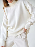 Rear view of a woman wearing an orange oversized turtleneck sweater and dark brown wide-leg trousers.